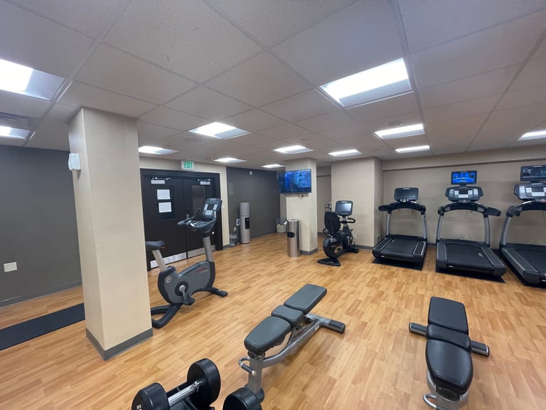 Modern gym interior with treadmills, stationary bikes, weight benches, dumbbells, and wall-mounted screens on wooden flooring