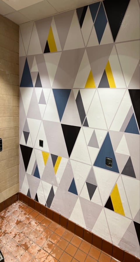 Modern geometric wall with triangular pattern tiles in white, gray, navy blue, yellow, and black colors in an institutional hallway
