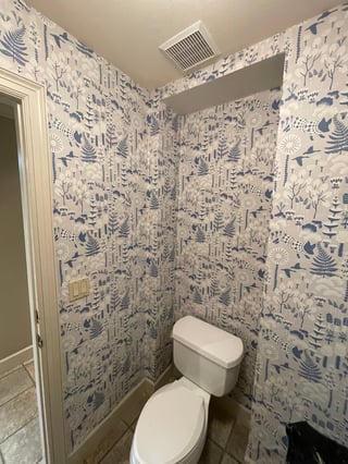 Small bathroom with blue and white botanical patterned wallpaper covering all walls and a white toilet