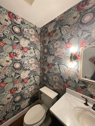 Bathroom with patterned wallpaper featuring red roses, black designs, and vintage elements, white toilet and sink with mirror