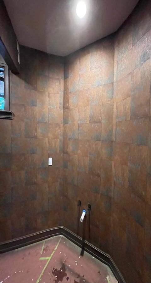 Interior view of a bathroom shower stall with brown tile walls, white ceiling light, and red tiled floor under construction