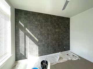 Bedroom with geometric patterned accent wall, white walls, window with blinds, and unmade bed with white linens