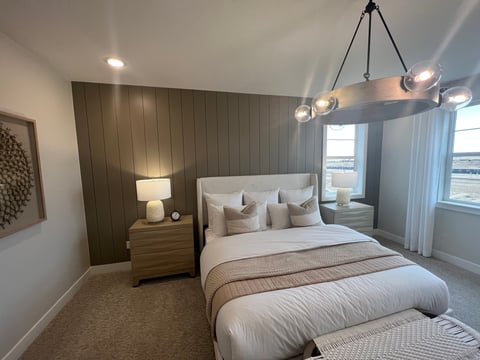 Modern bedroom with white bed, dark wood accent wall, pendant lighting, bedside table with lamp, and large windows with curtains