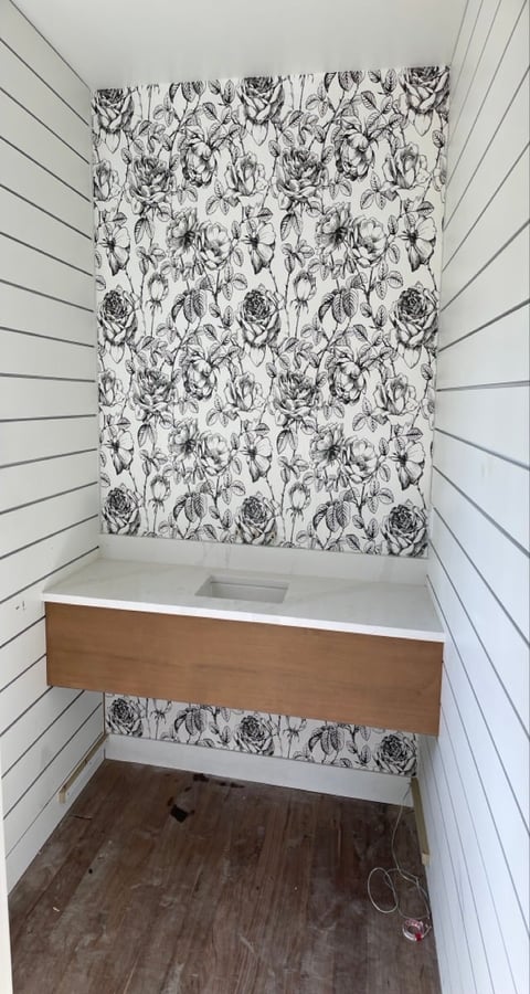 Bathroom under construction with white shiplap walls, black floral wallpaper accent wall, wooden vanity cabinet, and dark wood flooring