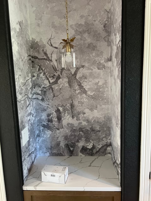 Empty glass pendant light hanging in a recessed wall niche with distressed concrete walls and a small cardboard box on the floor