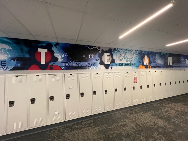 Row of white metal lockers in a school hallway with blue decorative wall mural above and modern ceiling lights