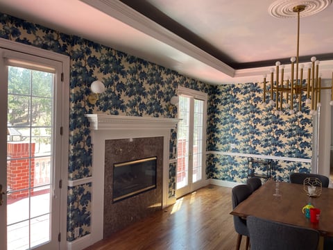 Modern dining room with navy floral wallpaper, fireplace, wood table, pendant lighting, and glass doors opening to an outdoor deck