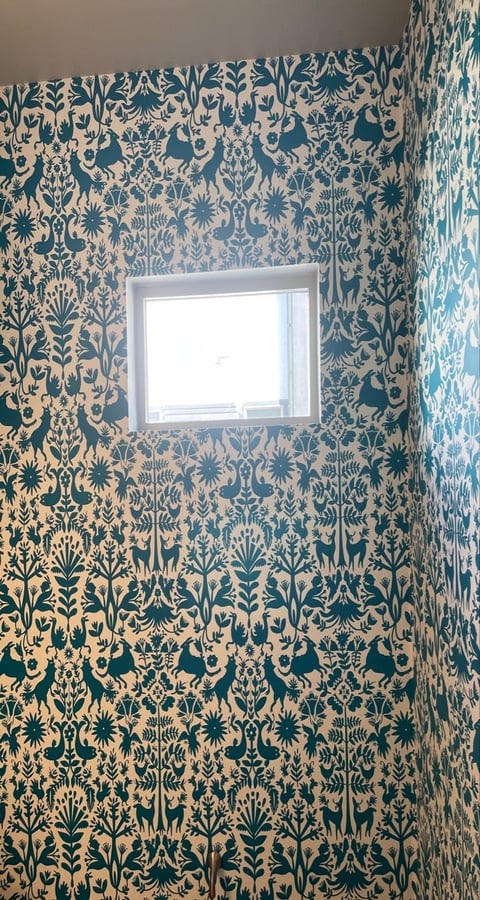 Bathroom with teal and cream damask patterned wallpaper covering walls, featuring white-framed window in center