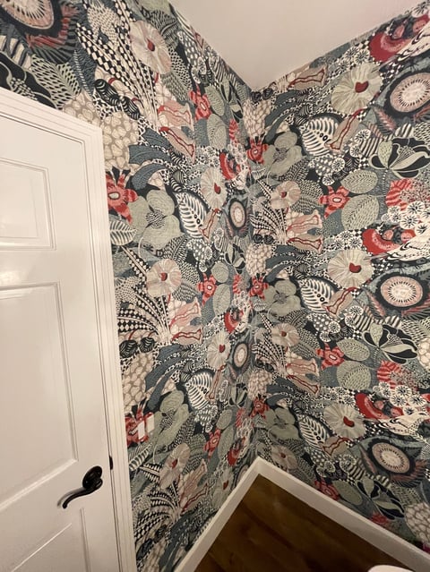 Corner of a room with bold patterned wallpaper featuring red, black, and gray botanical and geometric designs, white panel door with black handle visible