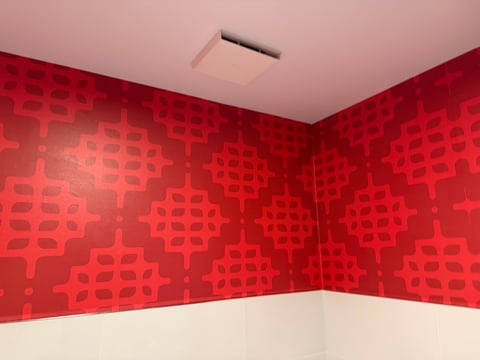 Corner of a room with red patterned wallpaper and white lower wall panels against a beige ceiling