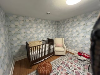 Nursery room with wooden crib, cream armchair, floral wallpaper, and patterned rug