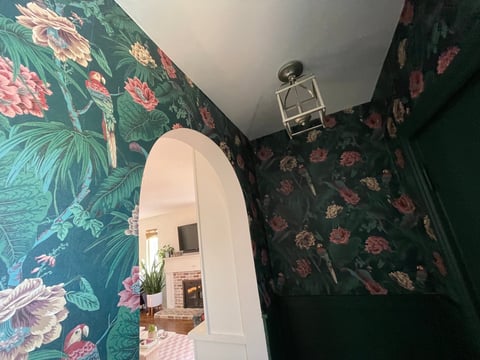 Bathroom with dark green floral wallpaper, white arched doorway, vintage light fixture, and glimpse of pink checkered floor beyond