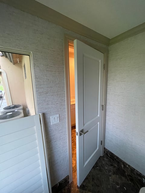 Interior hallway with gray textured wallpaper, white doors, and dark flooring leading to an orange-lit room
