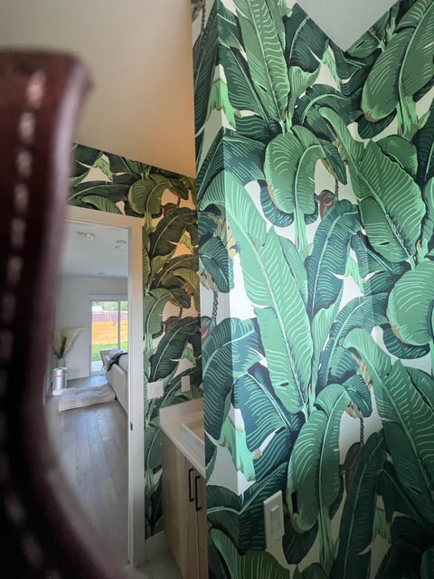 Interior hallway with vibrant tropical banana leaf wallpaper in greens and whites, leading to a bright entryway with staircase