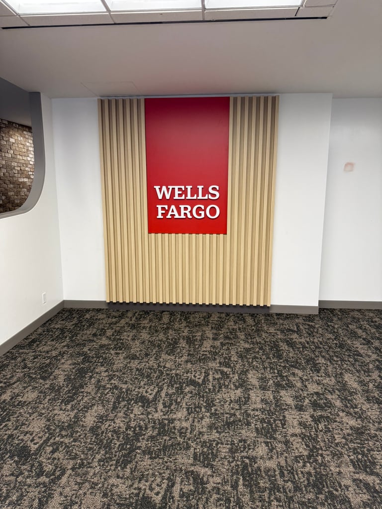 Empty Wells Fargo bank branch interior with red logo sign on fluted wall panels and gray carpet flooring