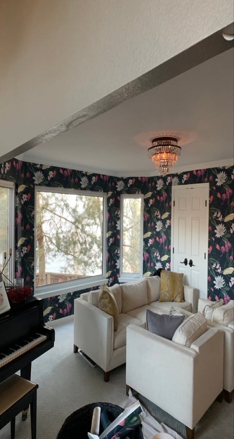 Modern sunroom with cream armchairs, floral wallpaper, large windows, piano, and decorative ceiling light