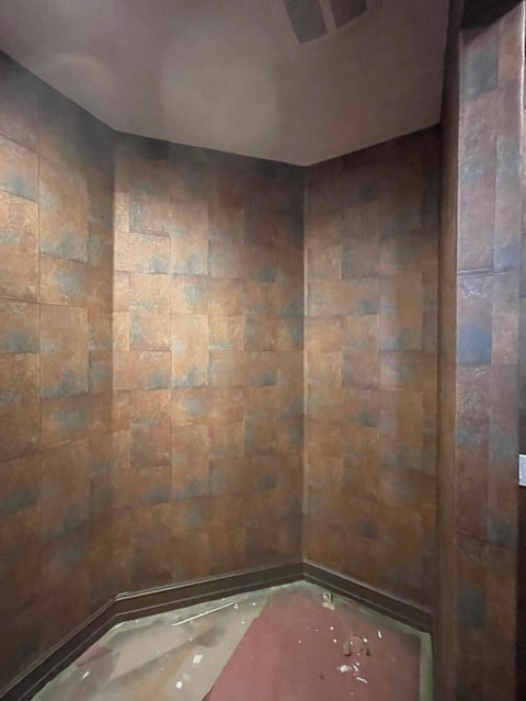 Empty shower enclosure with mixed brown and rust-colored tile walls and a glass door frame