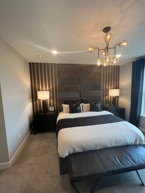 Modern bedroom with black upholstered headboard, white bedding, pendant lighting, and dark curtains
