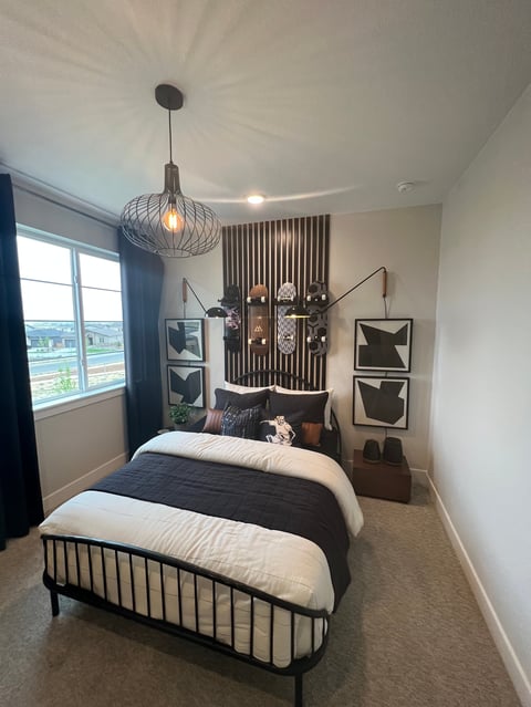 Modern bedroom with black metal bed, white and black striped bedding, pendant light fixture, and window with city view