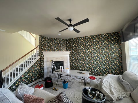 Bedroom with patterned wallpaper, ceiling fan, staircase, desk area, and scattered items on the floor and furniture