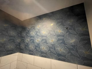 Modern bathroom with dark floral wallpaper above white subway tile wainscoting on two walls meeting at corner