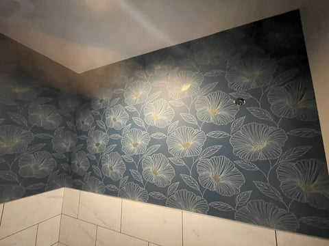 Modern bathroom with dark floral wallpaper above white subway tile wainscoting on two walls meeting at corner