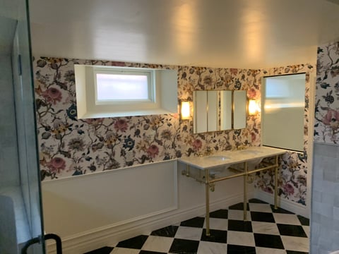 Modern bathroom with floral wallpaper, double vanity with mirrors, sconces, and black and white checkered floor