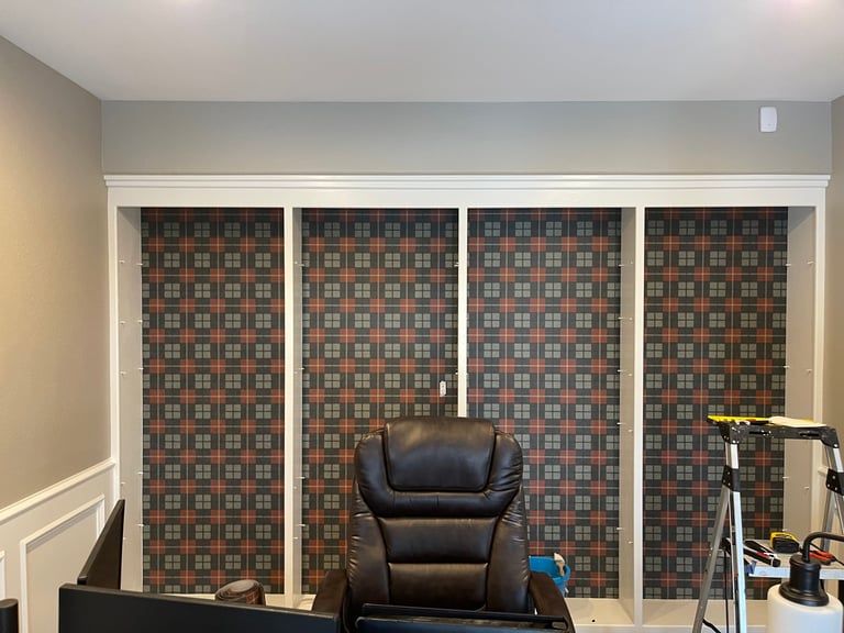 Black leather office chair in front of four panel closet doors with geometric patterned wallpaper in a home office space