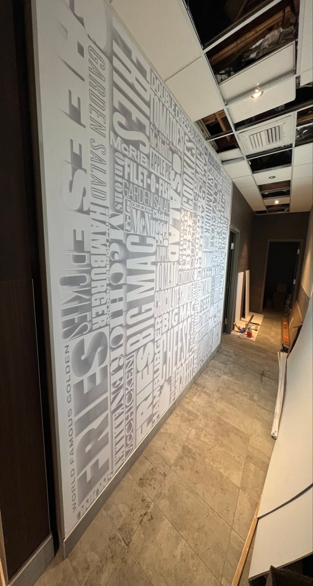 Large white wall mural with gray typography and text in an interior hallway with tiled flooring