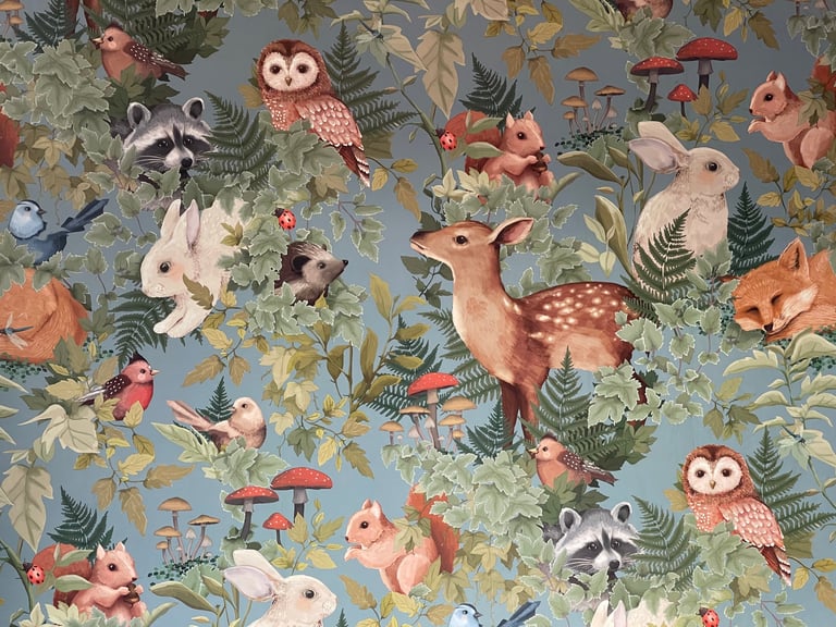 Woodland-themed fabric pattern featuring forest animals like deer, owls, raccoons, rabbits, and birds among green ferns and colorful flowers on a sage background