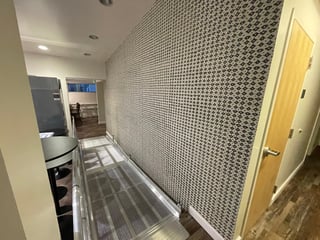 Modern kitchen hallway with geometric patterned wallpaper, recessed lighting, stainless steel appliances, and yellow door visible on right