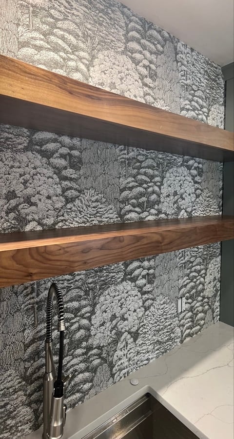 Modern kitchen backsplash with textured white and gray patterned tiles, three wooden shelves, and chrome faucet below