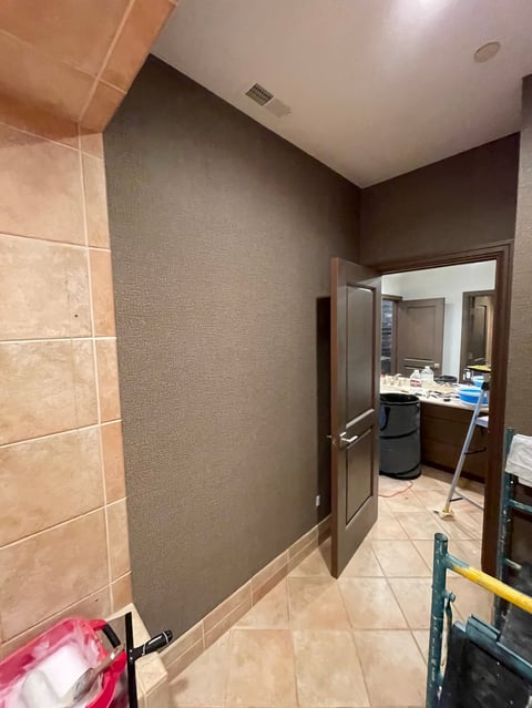 Bathroom with tan tile flooring, beige textured walls, dark brown accent wall, open doorway to vanity area, and white ceiling with vent