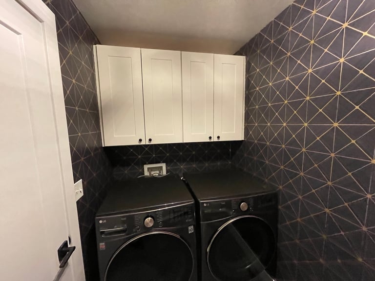Modern laundry room with white wall cabinets, black washer and dryer, and geometric patterned wallpaper