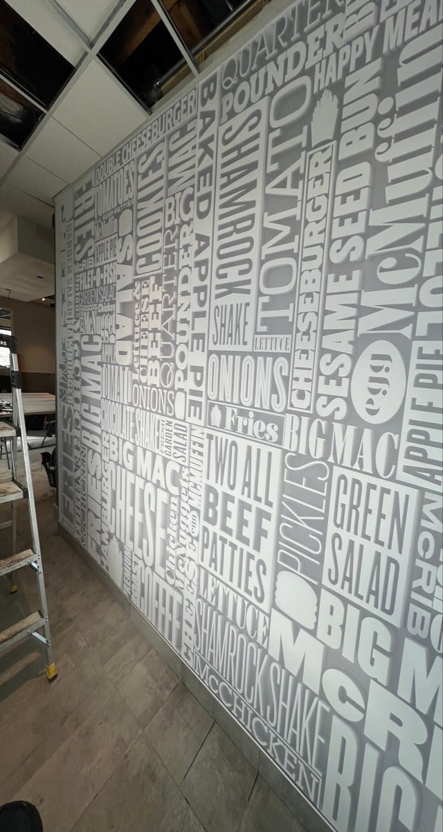 Large wall mural with white typography listing restaurant menu items and food descriptions in a modern cafe or restaurant interior