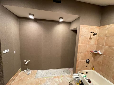 Construction-in-progress bathroom with unfinished shower enclosure, beige tile walls, recessed lighting, and plastic-covered floor