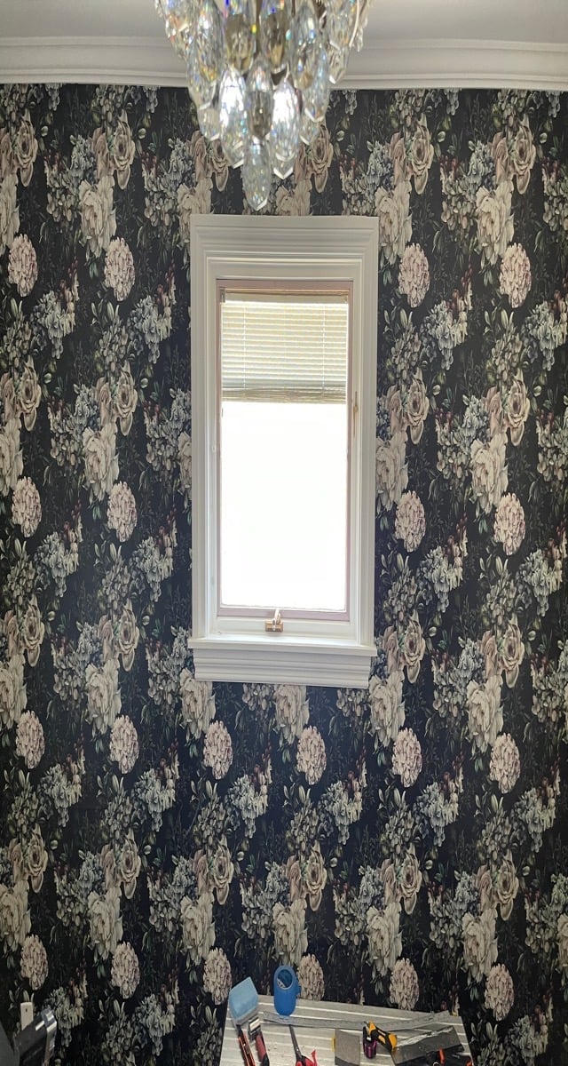 Elegant bathroom with dark floral wallpaper, white-framed window with blinds, and crystal chandelier overhead