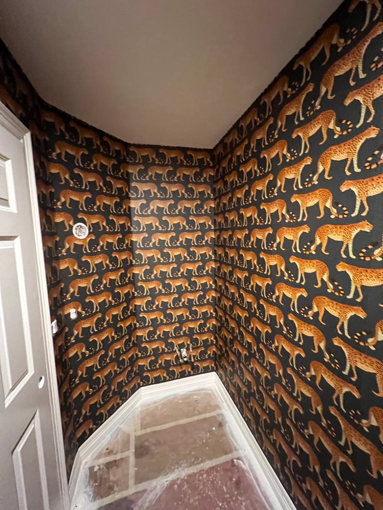 Corner of a room with black walls covered in repeating gold and orange animal silhouettes, white door and ceiling visible