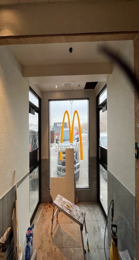 Interior view of a narrow McDonalds entryway with yellow arches visible through glass doors leading to the parking lot