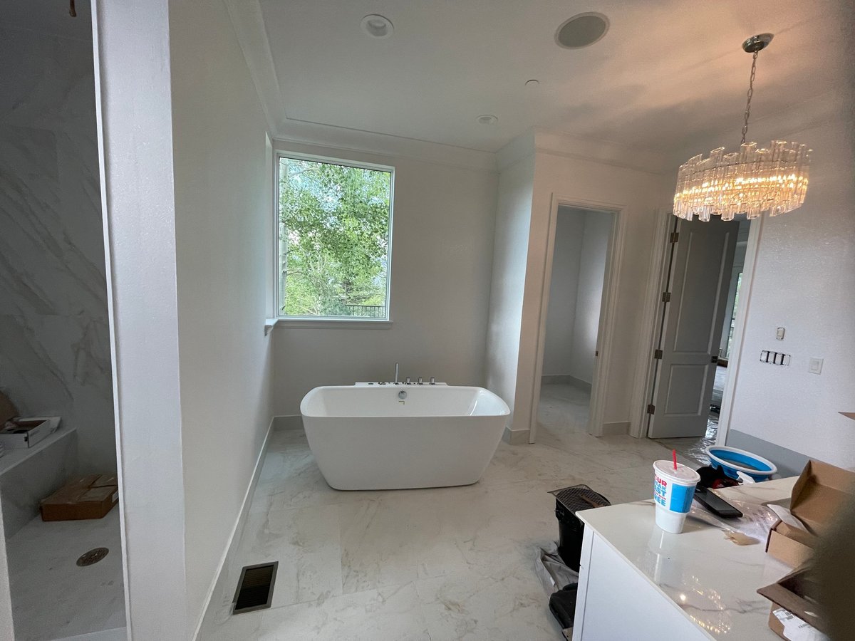 Modern bathroom under renovation with white freestanding tub, marble floors, chandelier pendant light, and construction materials