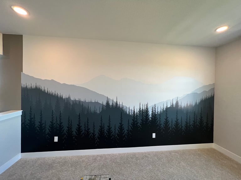 A room with a large wall mural depicting misty mountains and a dense forest of dark evergreen trees in silhouette against a light sky
