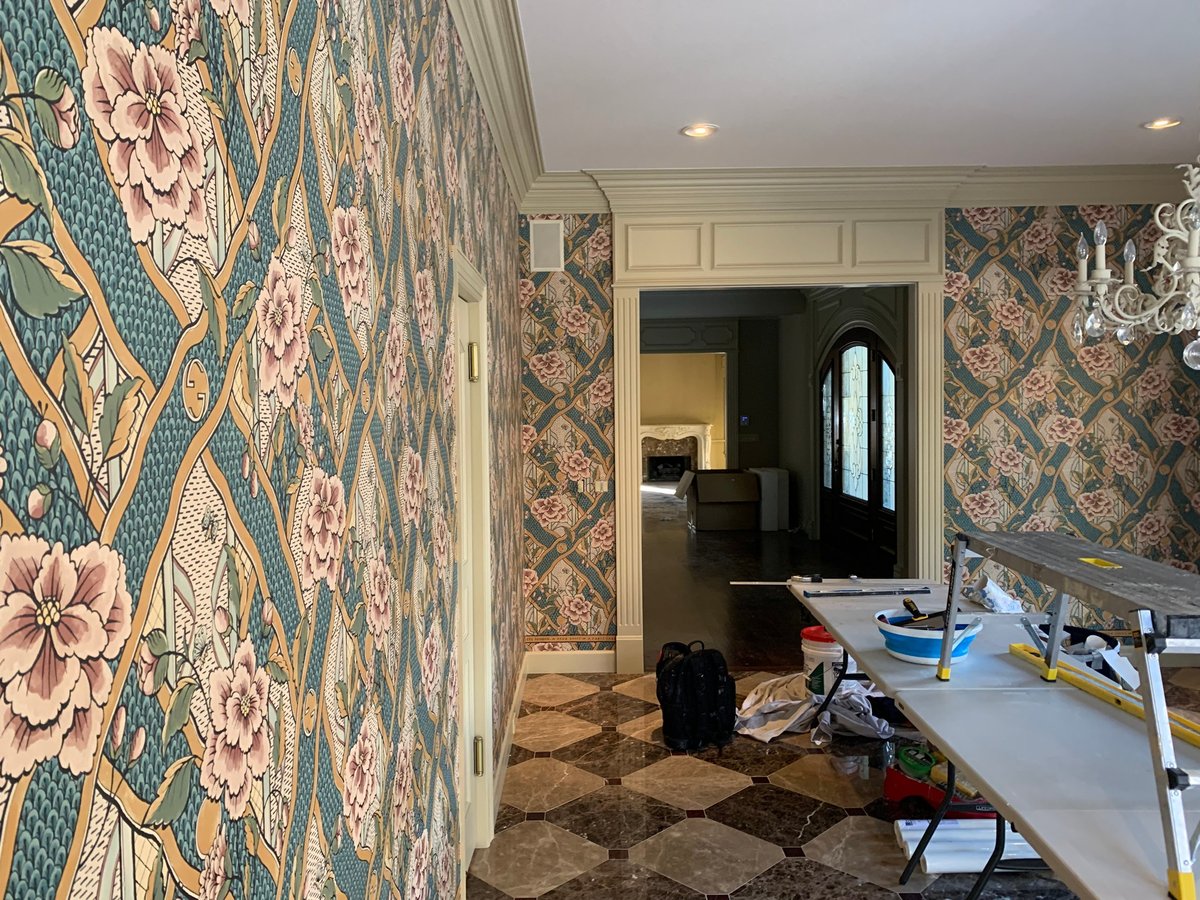 Interior of a bathroom with ornate floral patterned wallpaper in teal and pink tones, vanity sink, and doorway to adjacent room