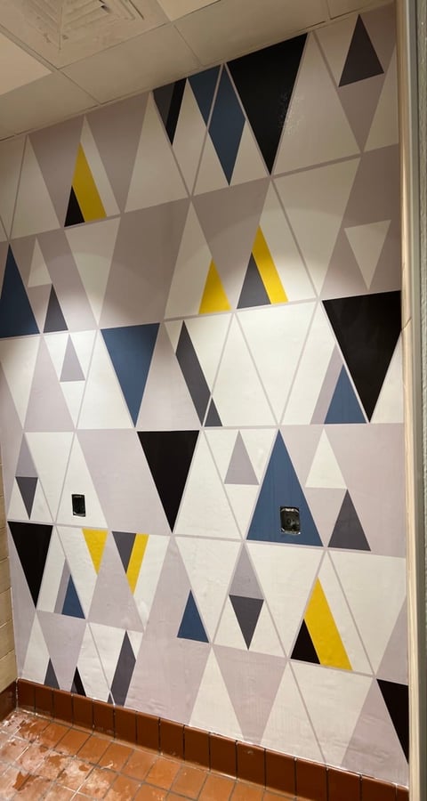 Modern geometric wall mural with white, black, gray, blue, and yellow triangular tiles in a pattern on an interior wall