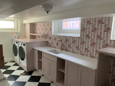 Modern laundry room with two front-load washers, white cabinetry, bird-patterned wallpaper, and black and white checkered floor