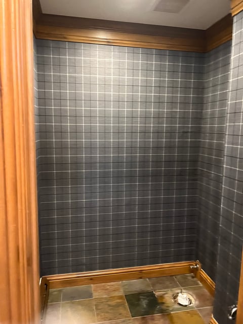 Shower stall with dark gray tile walls, wooden trim, and orange curtain rod with partial curtain visible