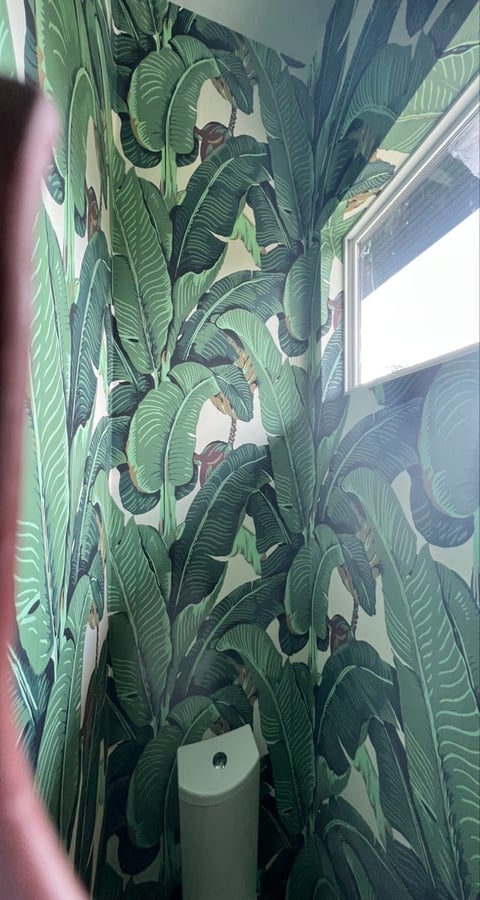 Bathroom corner with tropical banana leaf wallpaper in shades of green, featuring a white toilet base at bottom